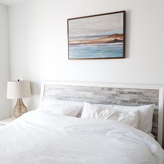 Bed with white sheets and a picture of the ocean hanging on the wall over the bed.