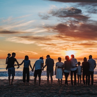 People holding hands on a beach facing the sunset