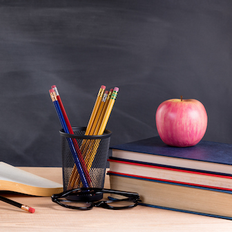 A teacher's desk with an apple, books, and pencils