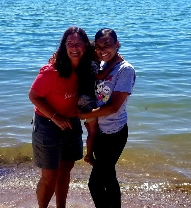 Photo of Destiny and Becca holding Jayden on the beach