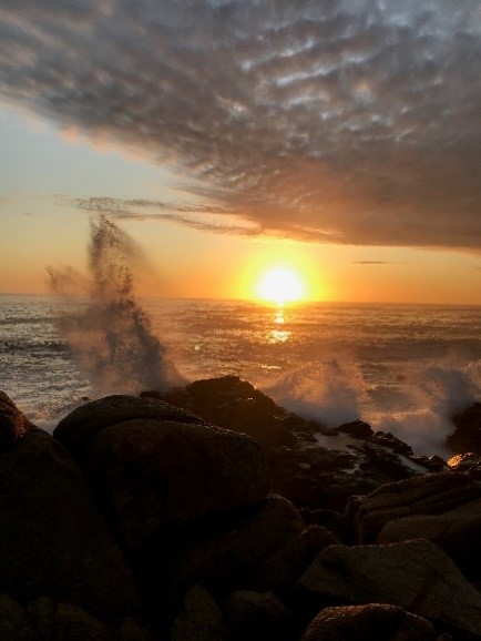Photo of a sunset next to a body of water as a wave crashes