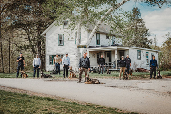 Officers and K9s standing in front of a white farmhouse.